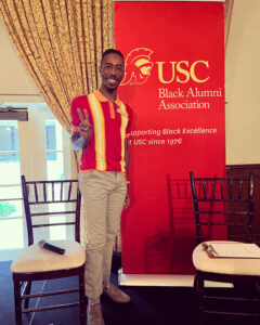 DMM graduate Terrell M. Green standing and smiling in front of the USC Black Alumni Association sign.